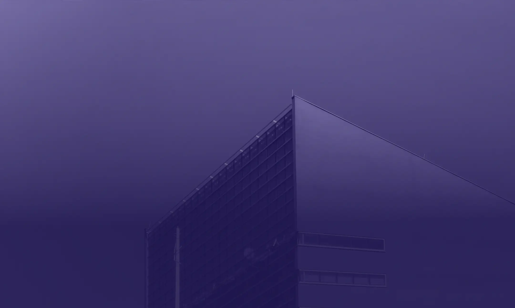 A modern building with sharp, angular lines and a glass facade is set against a gradient blue sky. The image reflects the essence of our "about us" ethos in a purple monochrome tone, giving it a serene and minimalist ambiance.