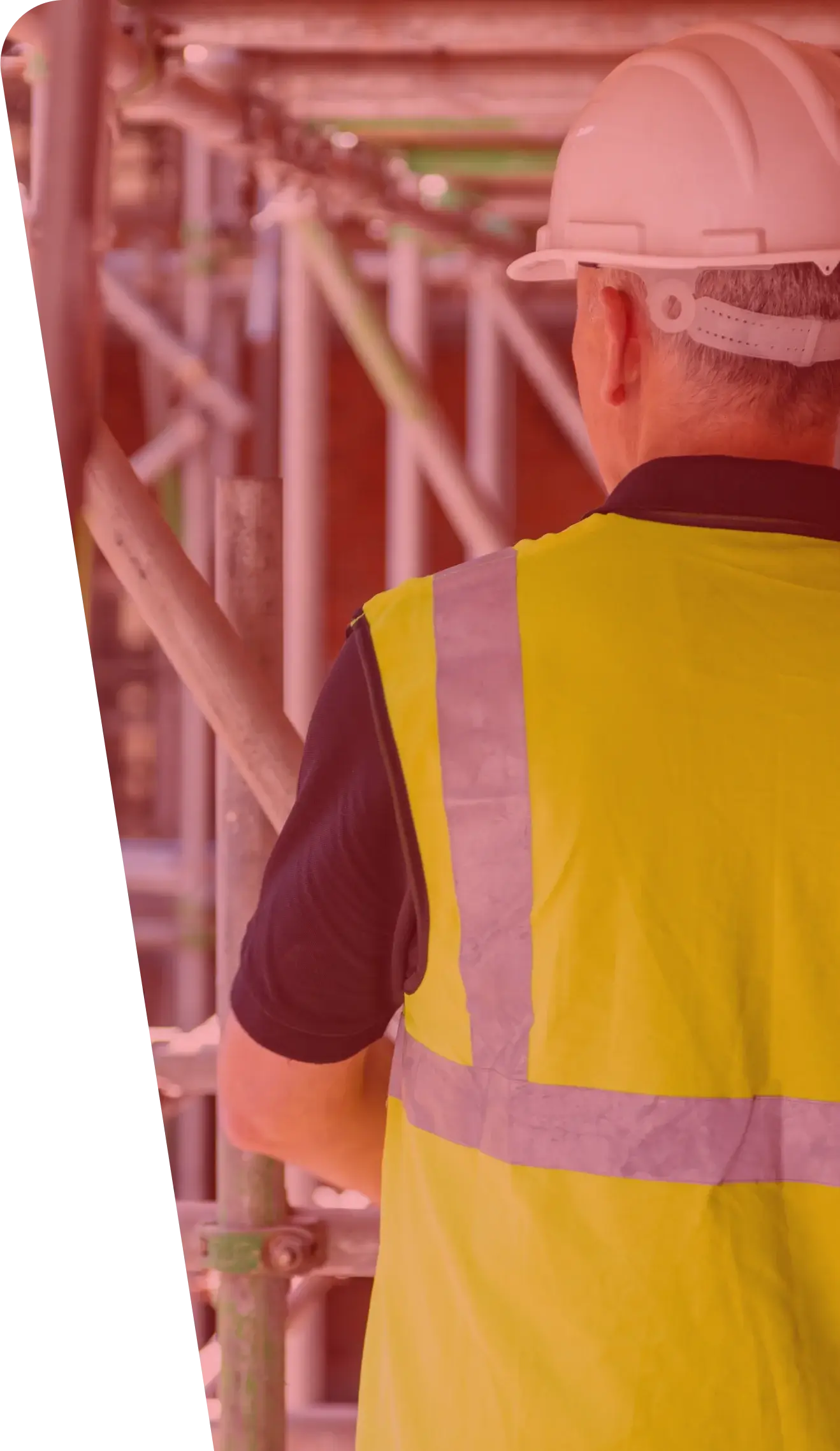 A construction worker wearing a white hard hat and a yellow high-visibility vest stands facing scaffolding. The worker's back is to the camera, actively interacting with the structure on-site, ensuring that the services provided meet safety standards in this bustling construction zone.